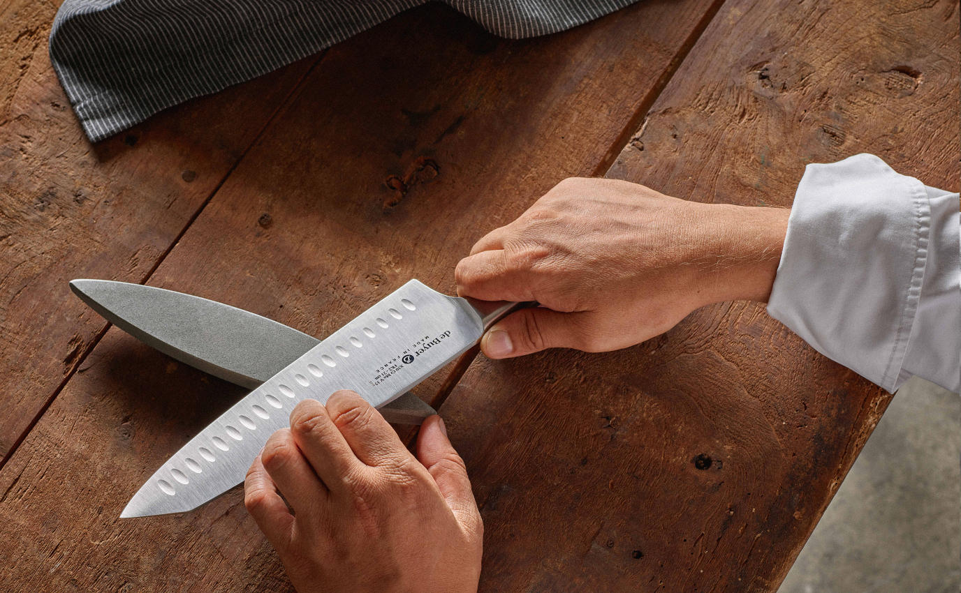 Photographie couleur mains d'homme en gros plan qui fabriquent un couteau de façon artisanale sur une table en bois vieilli pour De Buyer - Frappa Studio ©2018