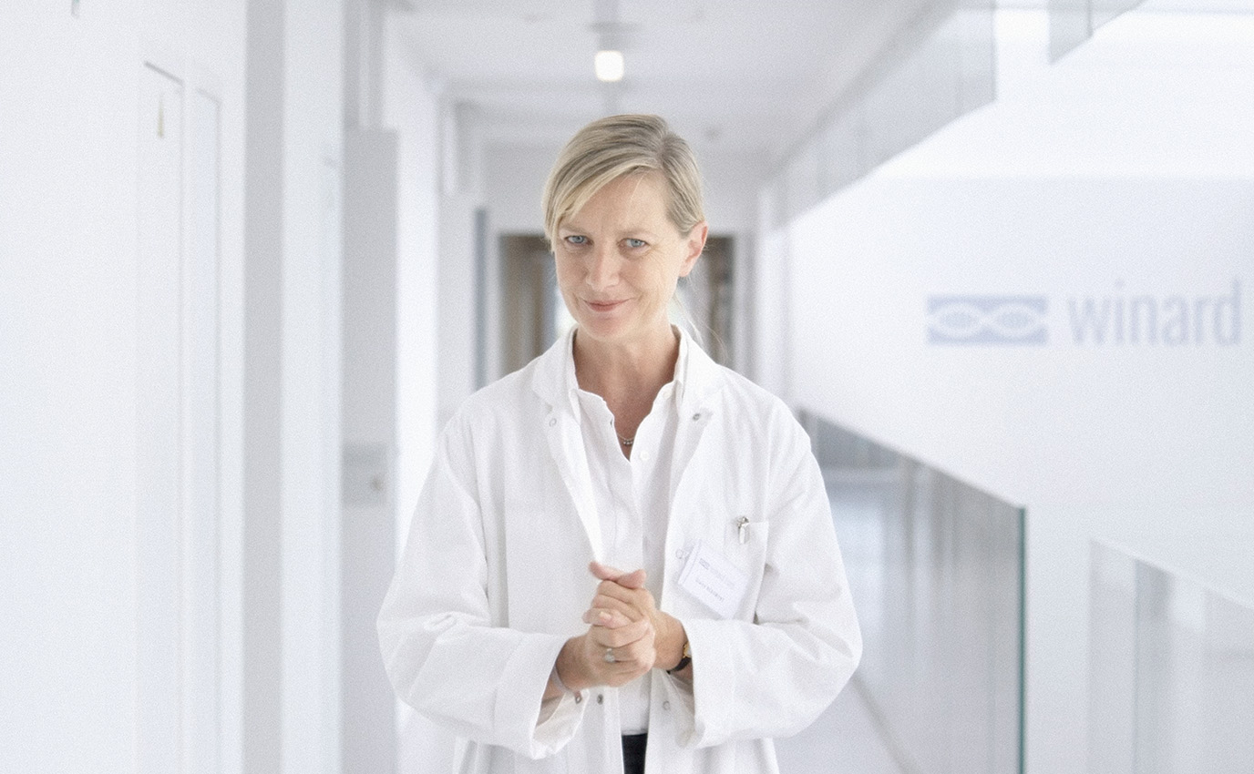 Photographie couleur d'une femme médecin inquiétante qui se frotte les mains en nous regardant dans un grand laboratoire lumineux et futuriste pour Discovery Science - Frappa Studio ©2015