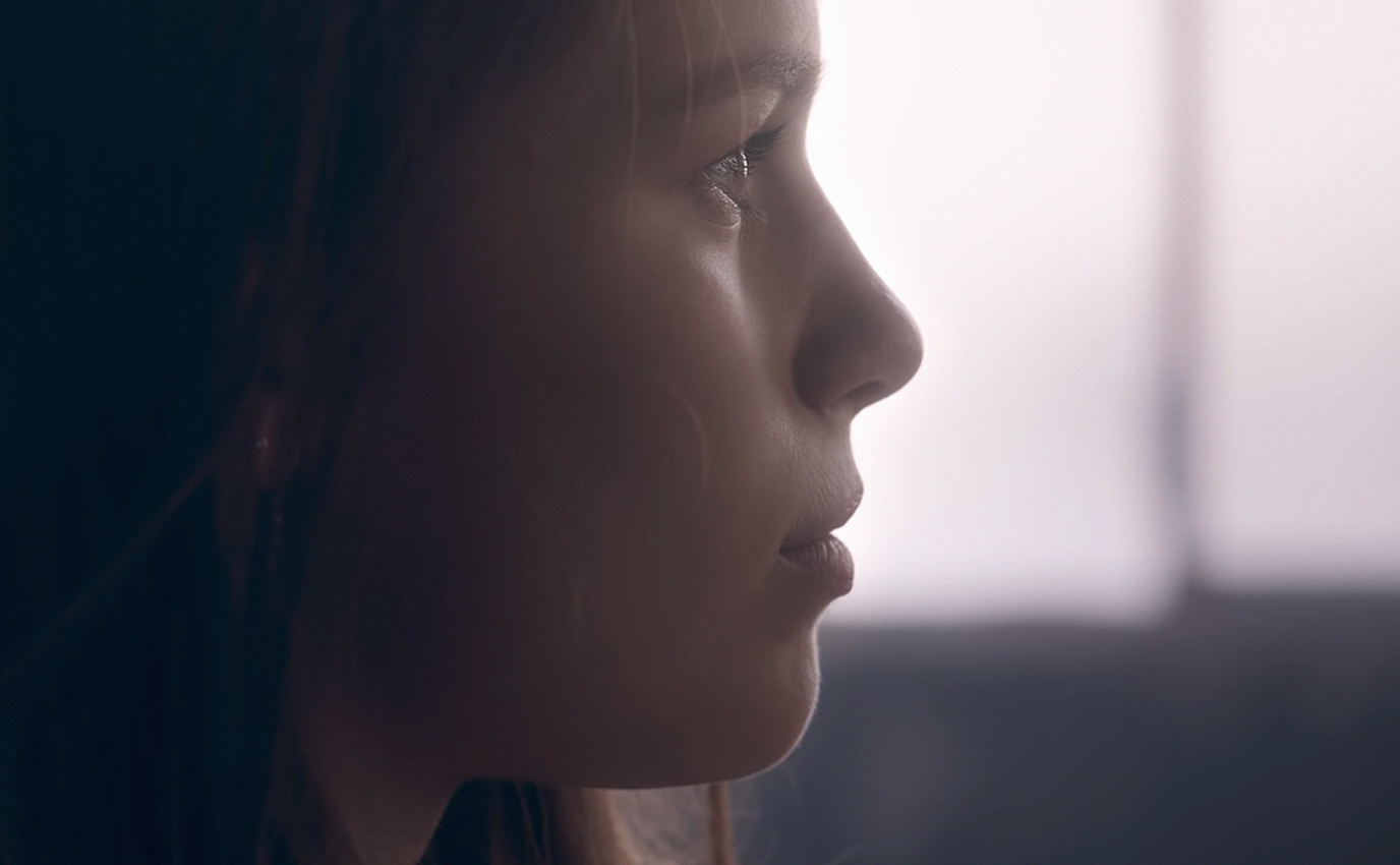 Photographie couleur en contre-jour d'une jeune femme silencieuse et pensive, de profil en très gros plan extraite du film pour Vaincre le Cancer - Frappa Studio ©2019